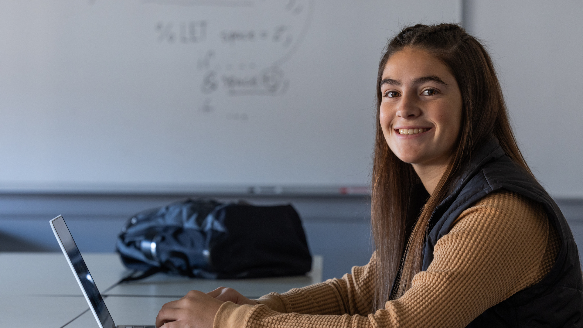 A student smiling to camera, sitting at a laptop