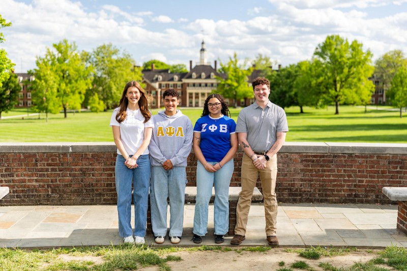 Four students in greek letters, posing in front of central quad.