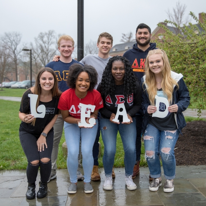 Students holding up white letters that spell out "LEAD" in front of the sundial.
