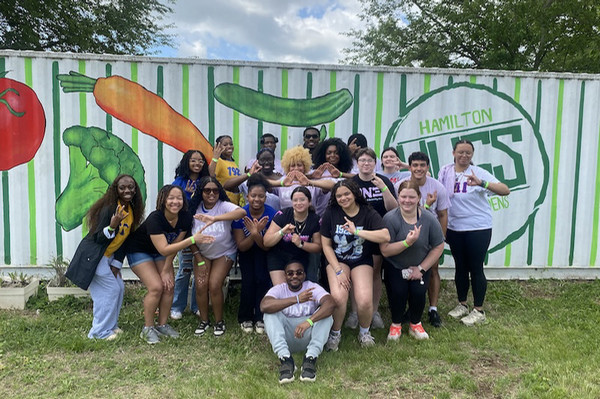 Large group of greek students posing in front of a fence painted with a mural.
