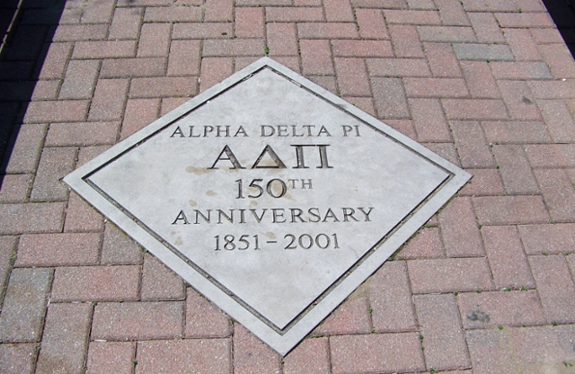 Diamond shaped concrete seal in the ground that reads Alpha Delta Pi 150th anniversary. 1851-2001.