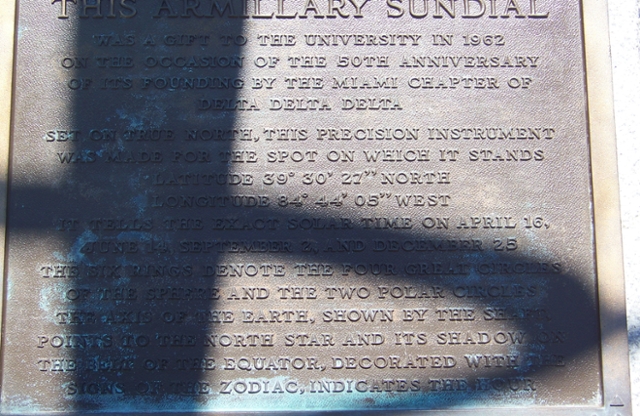 Plaque with shadow blocking some of the text. Text reads This armillary sundial was a gift to the university in 1962 on the occasion of the 50th anniversary of its founding by the Miami chapter of Delta Delta Delta.