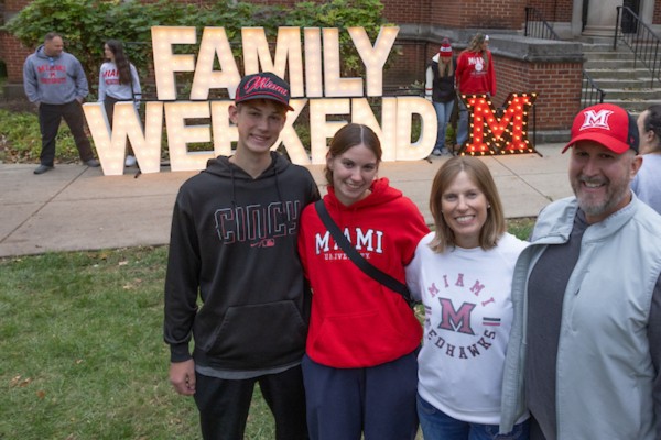 A family posing in front of large light up letters that spell Family Weekend.