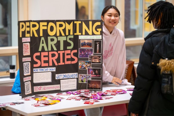 Students working behind a table with a trifold that reads Performing Arts Series.