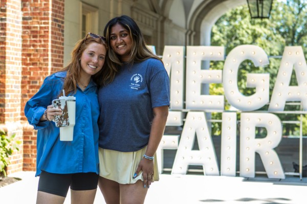 Two students posing in front of a large light up letter sign reading Mega Fair.