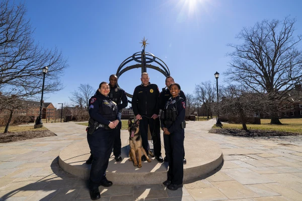 multiple police officers with police k-9 in front of sundial