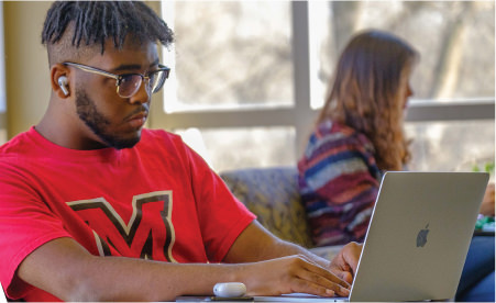 an image of a student working on a laptop wearing Miami red