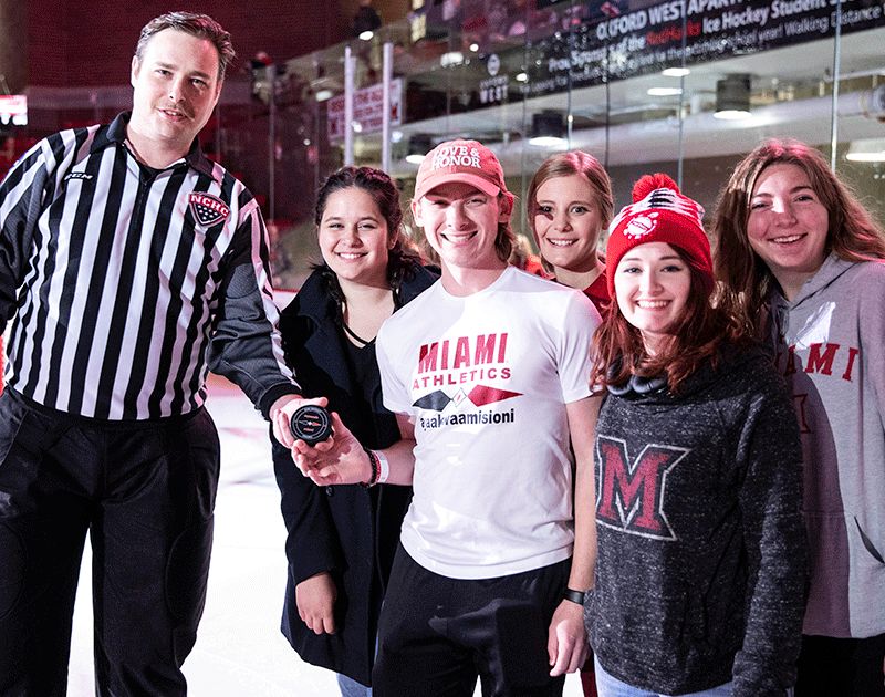 myaamia students at a hockey game holding the game puck with the referee