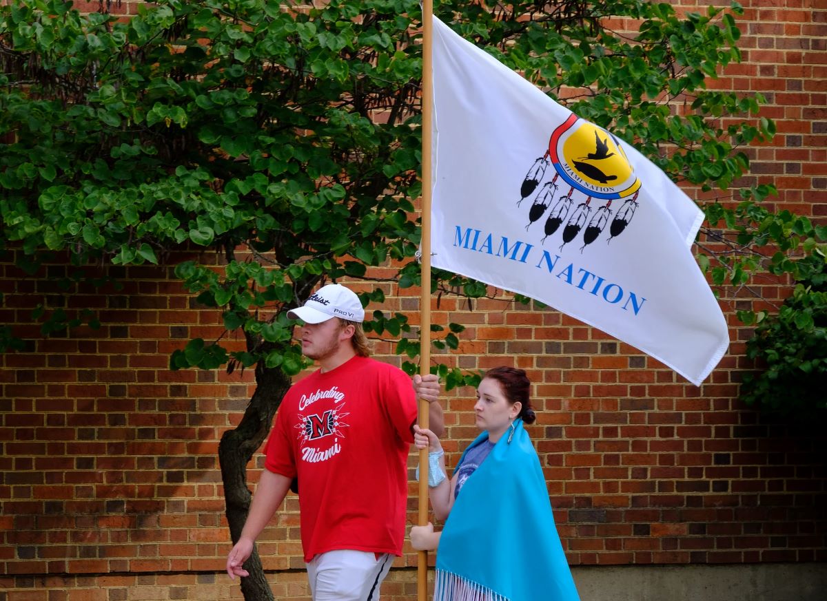 Myaamia students holding the Miami Nation flag while walking on the path of reflection across Miami's Oxford campus
