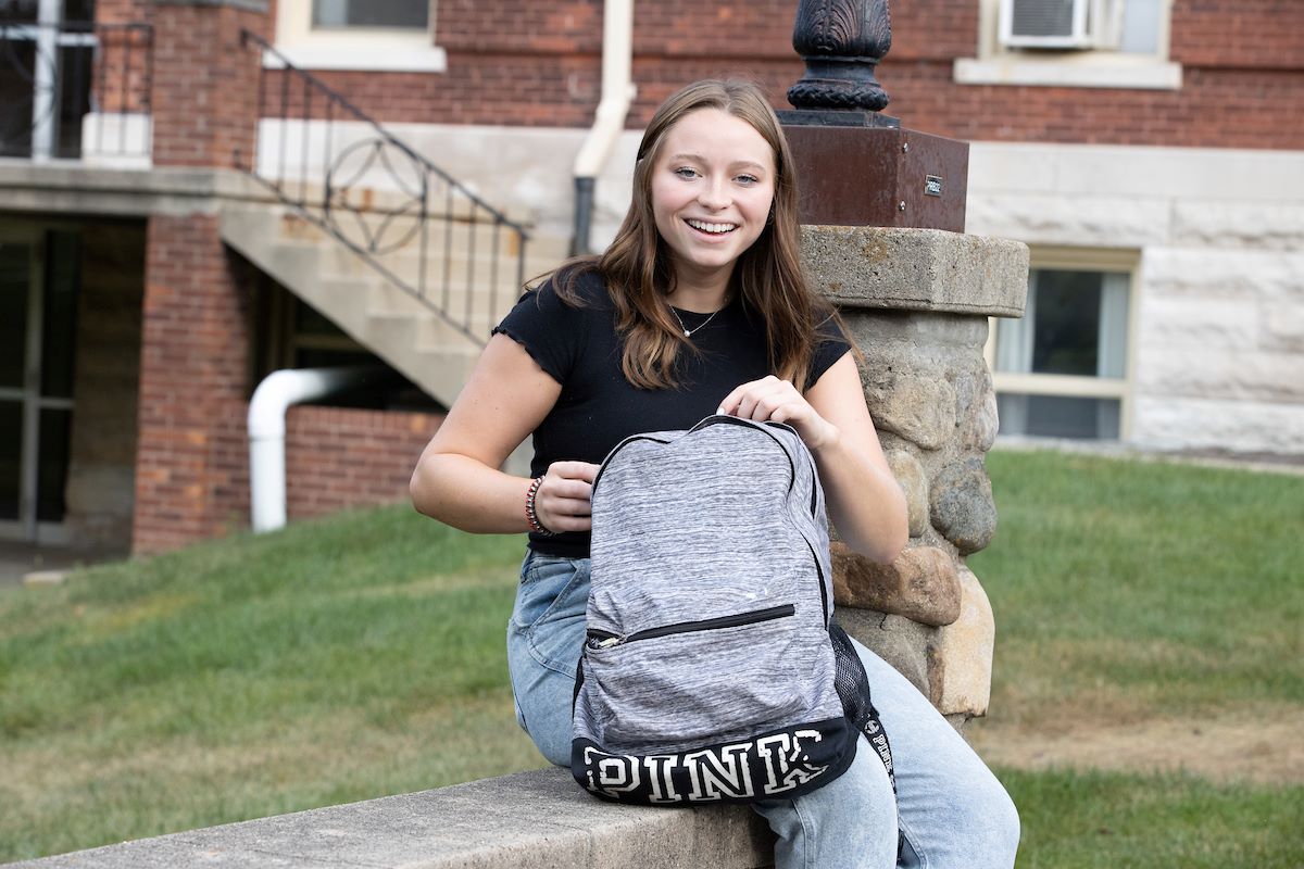 Abbey Stoltzfus sitting on a bridge on Miami's Oxford, Ohio campus unzipping her backpack