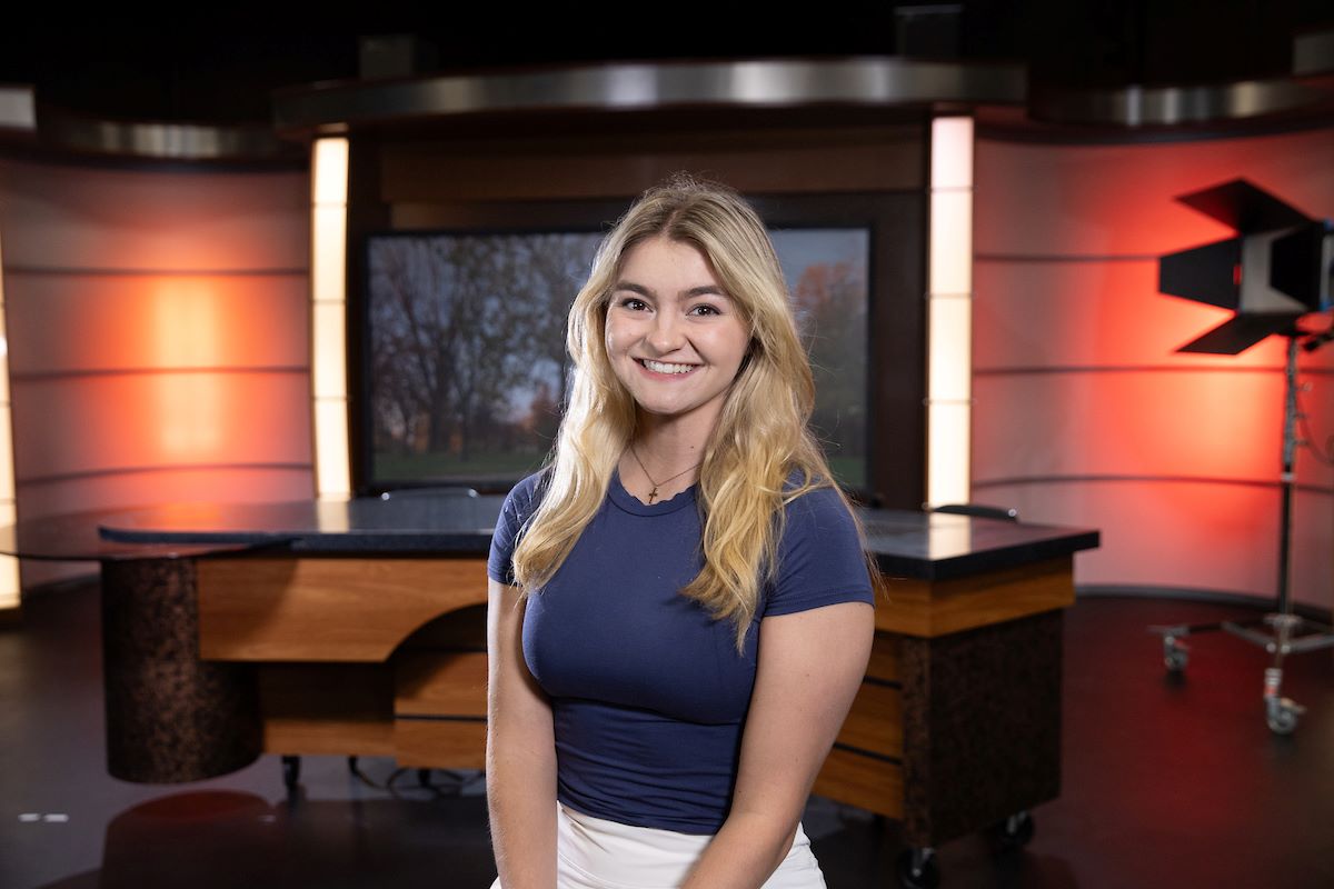 Abby Rineer standing in front of a news room filming studio