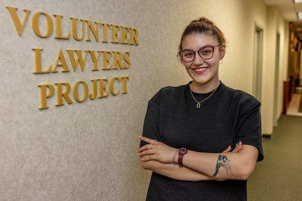 Anastasija standing next to a sign for the Volunteer Lawyers Project at the office entrance