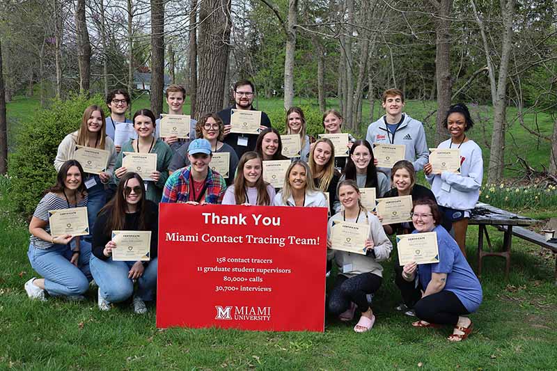 A group of students, IT staff, and public health faculty gathered at Miami's Dogwood Grove with a thank you sign 