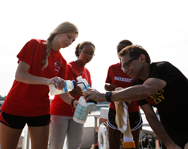 Mike Vanni (right) holds up a water sample for 3 students, on a pntoon boat in Acton lake