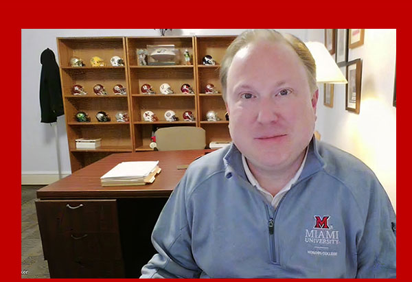 Zeb Baker in his office with display case of miniature helmets behind him