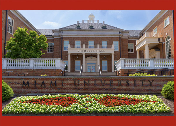 red and white flowers in a planting bed the shape of Miami Tribe relationship logo in front of Shideler Hall