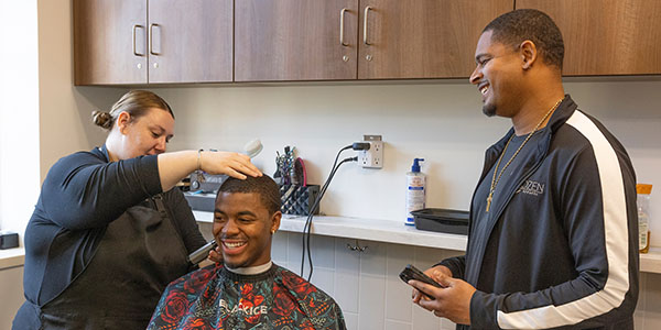 Taylor Millard cuts the hair of a student as Razor Sharp barbershop owner Marquan Richardson talks to them