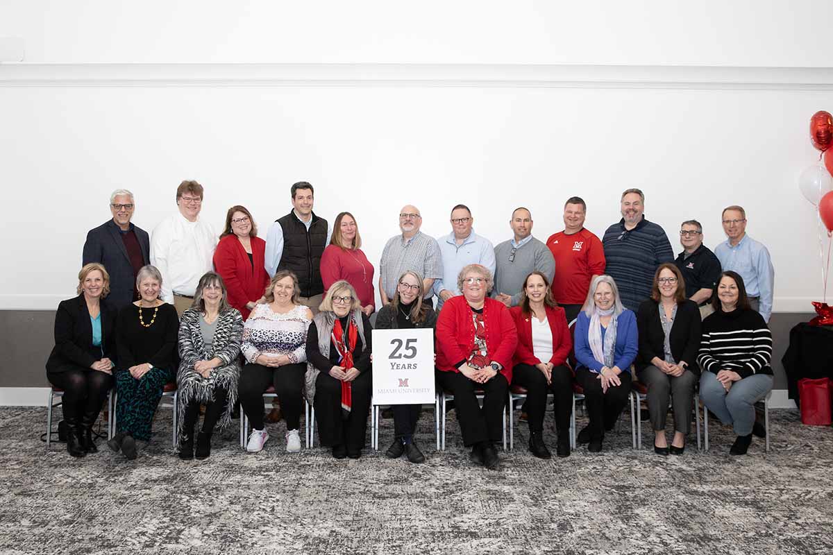 A large group of Miami employees pose with a 25 years of service sign in the Dolibois room