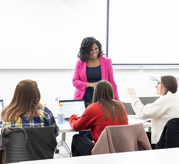 Amber Franklin in a classroom talks with 3 students sitting at tables