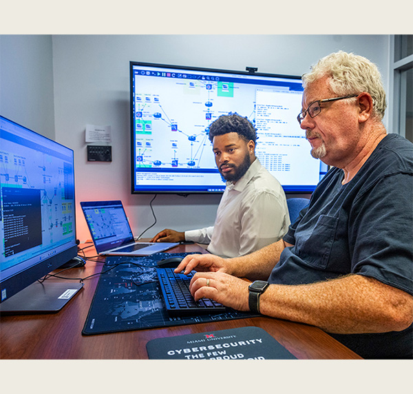 two people sit at a table , each works on a laptop computer