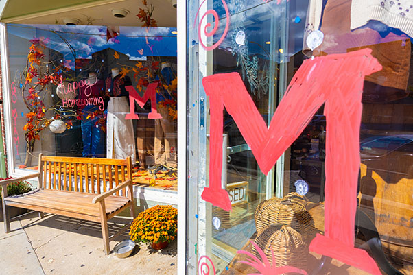 Two red block Ms on a storefront window and the words Happy Homecoming