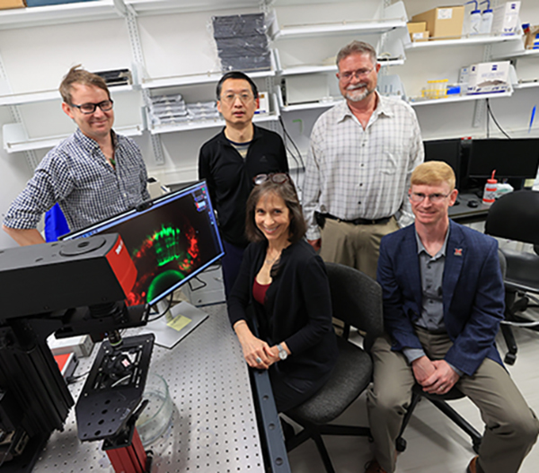 Mark Charlton-Perkins, Hui Wang, Mike Robinson , Katia Del Rio-Tsonis and Andrew Jones pose next to a microscope and monitor in a research lab