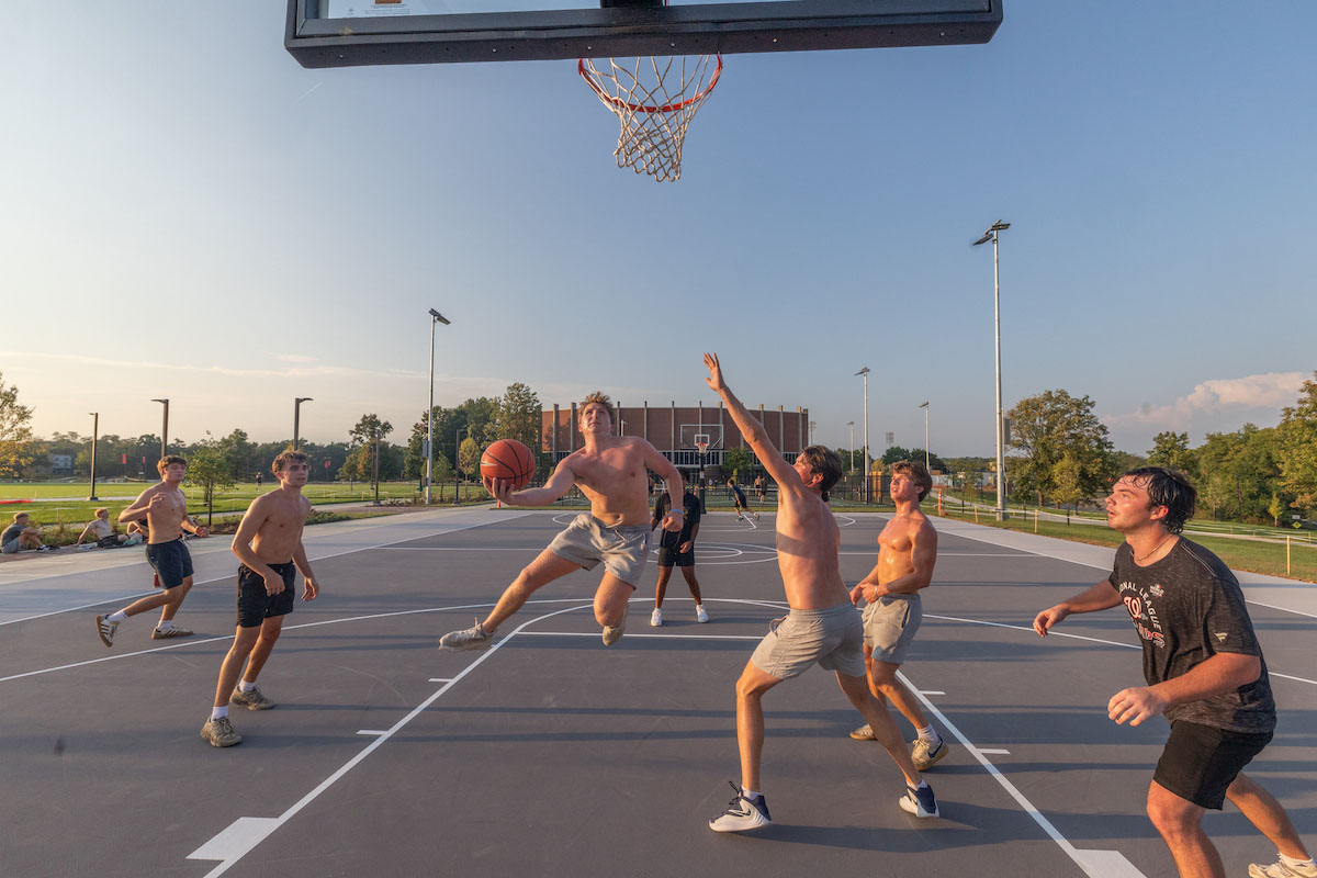 a group of sweaty students play basketball at an outdoor court near Millett