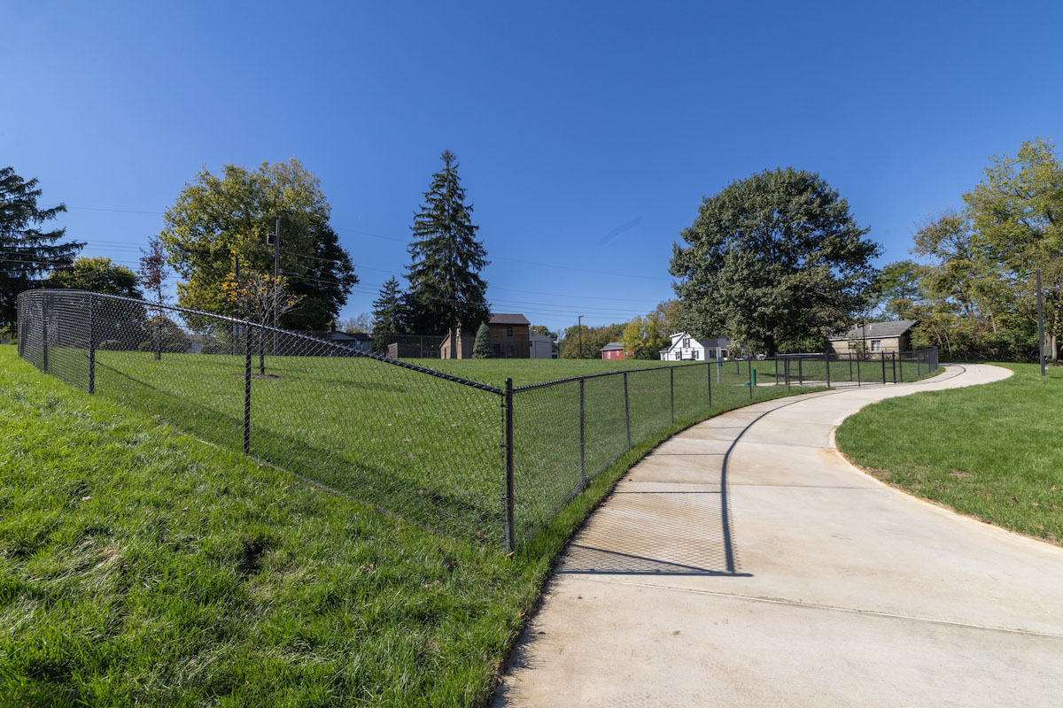 a grass covered area fenced in as a dog park with a cement path next to it