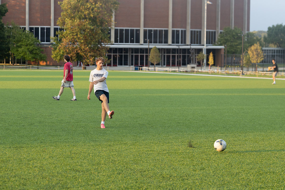 A student kicks a soccer ball on the new field near Millett hall 