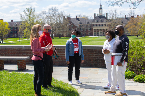 President Greg Crawford and Dr. Renate Crawford talk to a visiting family near the Sundial plaza with MacCracken Hall in the background.