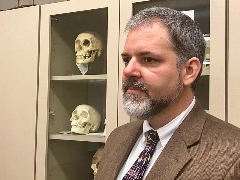 Jeb Card stands near a display of archaeological skulls