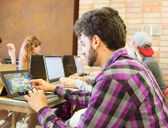 A student touches a screen as others work in the gaming lab