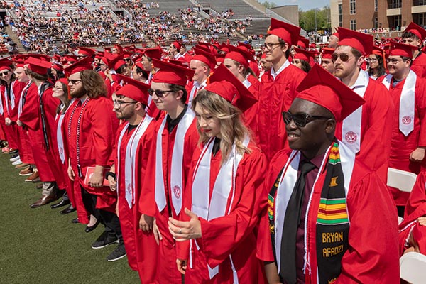 Graduates smile while standing in their row at a commencement ceremony.
