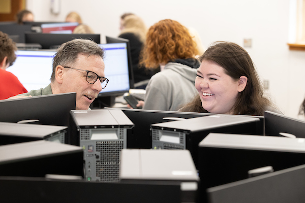 An advisor and student chat over a computer in a computer lab.