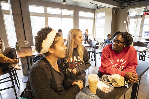 Three Miami students talk in a cafe.