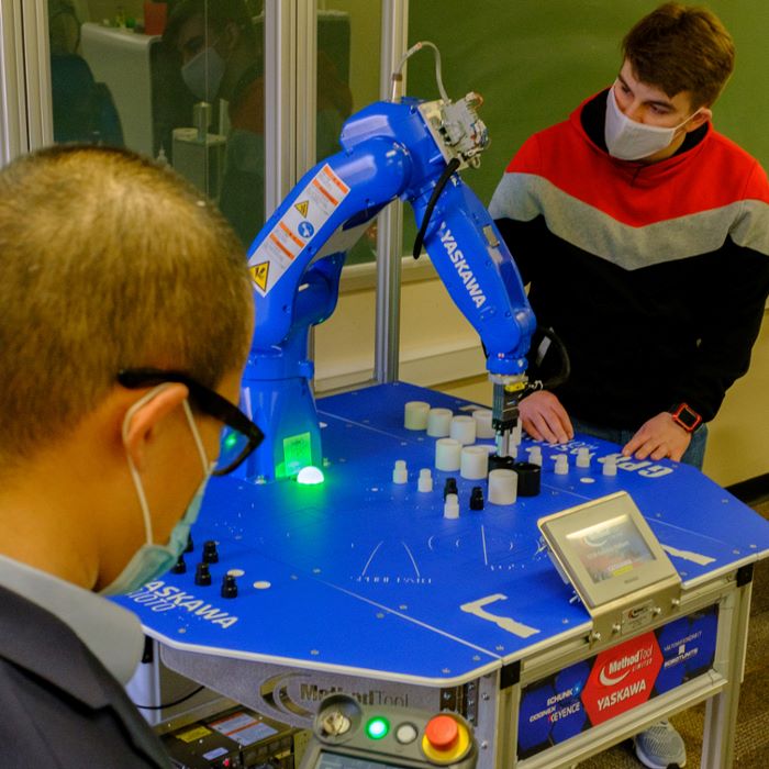 Two students working with a blue robotic arm