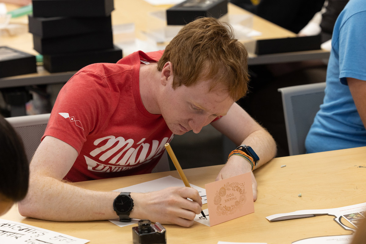 A student writes a thank you card at a desk.