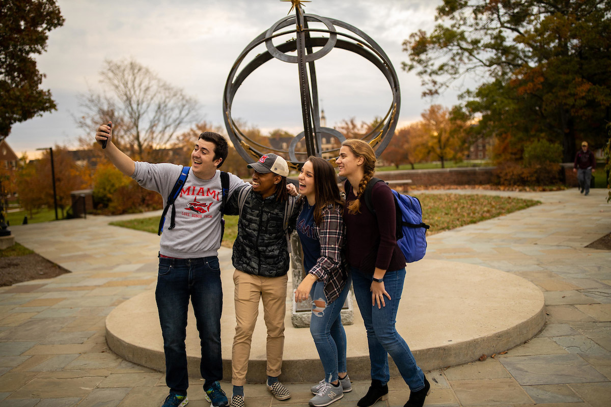 A group of students take a selfie in front of the Tri-Delta Sundial.