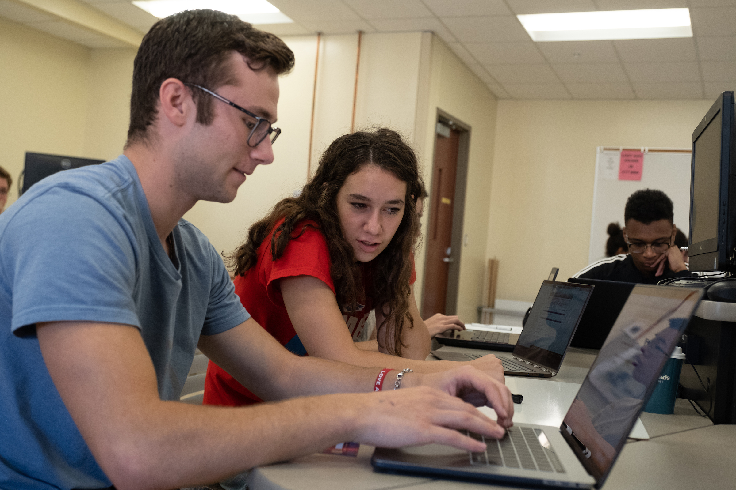Two students work on laptops while sitting in a computer lab..