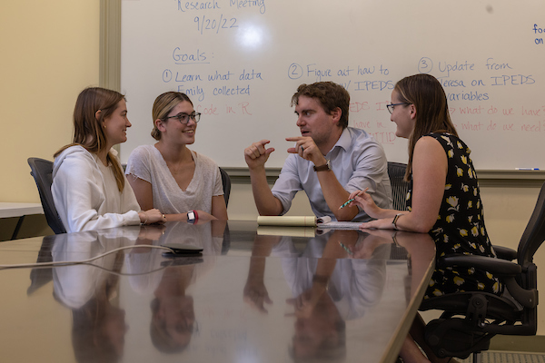 Three students talk with a professor at a conference table.