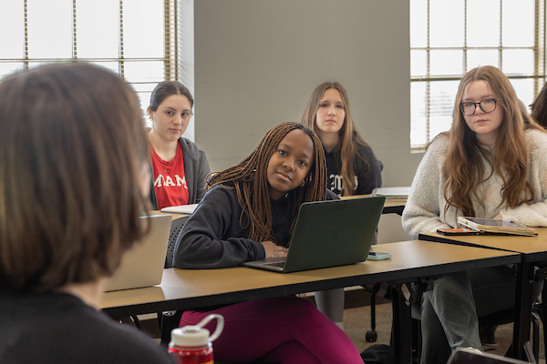 Four students listen to a professor speak in class.