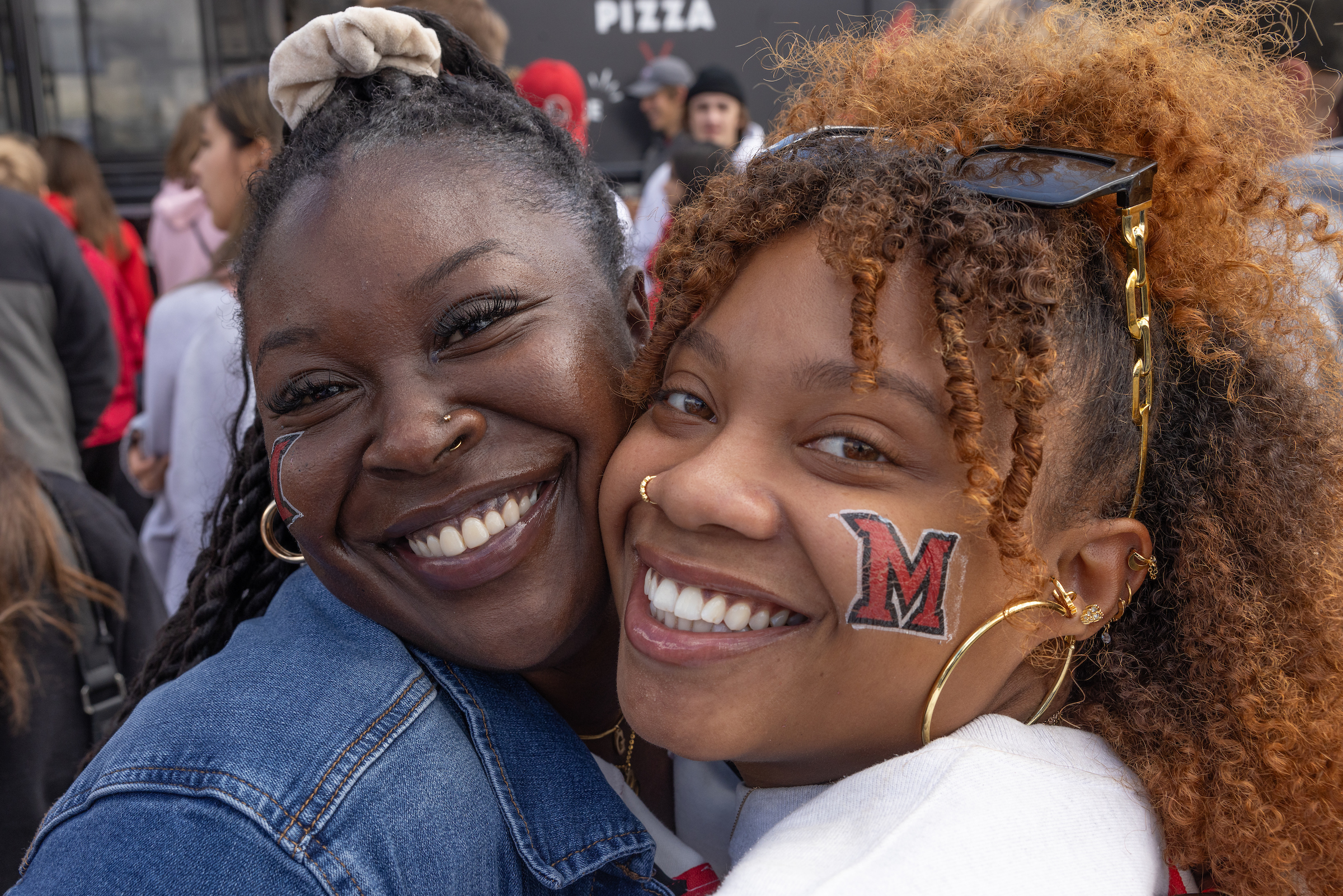 A student and parent pose for a picture, each with a Miami M temporary tattoo on their cheek.