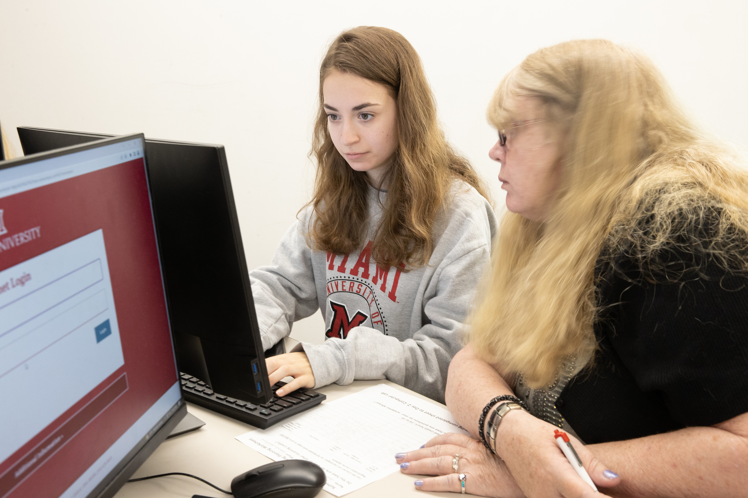 A student works on a computer as an advisor looks on.