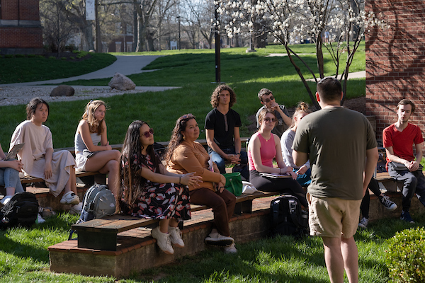 A professor addresses a group of students outside.
