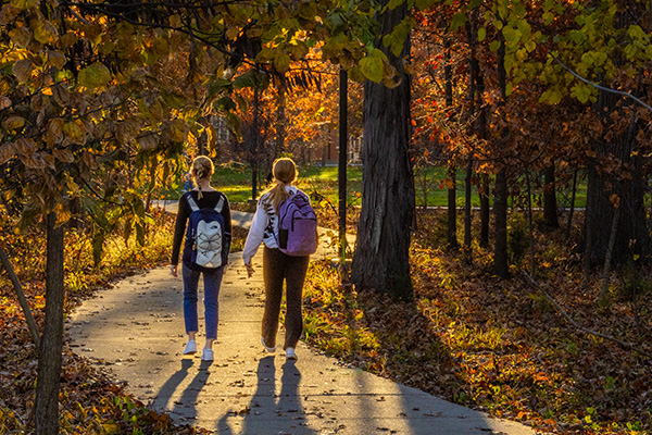 Students walk to class in the fall, with one riding a bicycle.