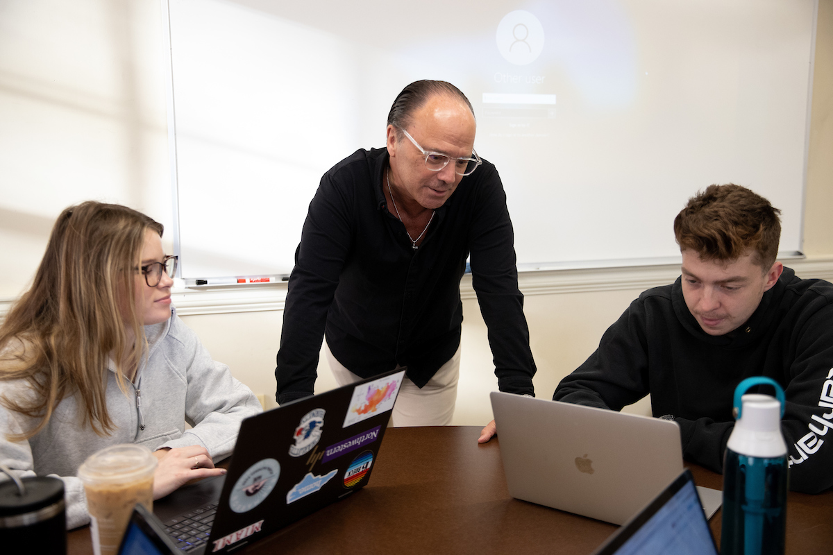 Two students and a professor talk around a table.