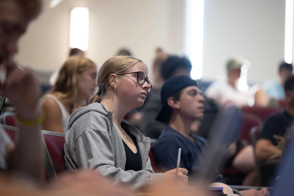 A student takes notes in class while surrounded by peers.