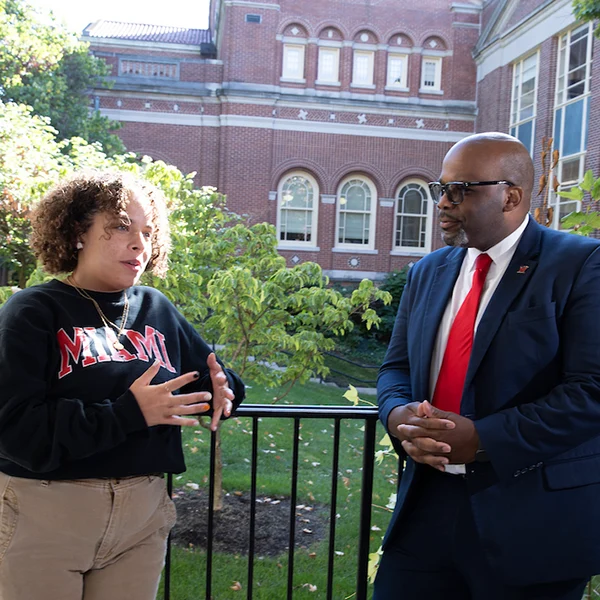 A leader in student affairs is talking to the student government president in with campus landscape in the background.
