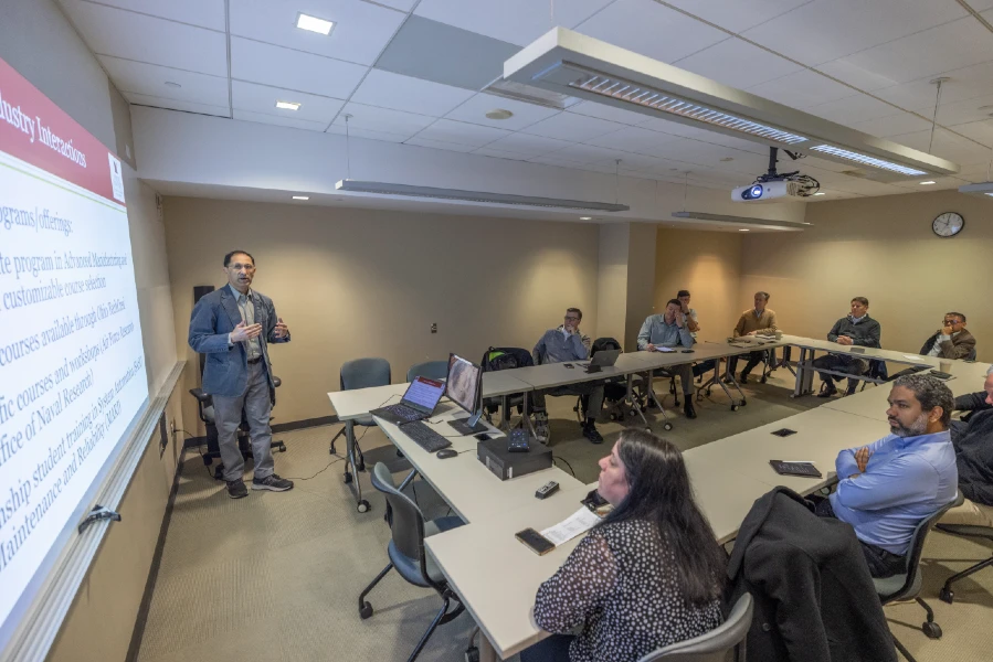 professor presenting to group of students in classroom with table shaped in a u 
