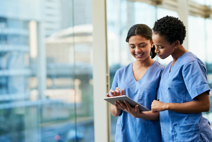 two nurses standing together wearing blue scrubs looking at a chart